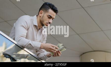 Junger lateinamerikanischer geschäftsmann, bärtiger Typ mit Dollars, stapeln Geldscheine und zählen Geld. Nahaufnahme Männchen zählen Bargeld auf dem Balkon. Konzept für Gehaltszahlungen Stockfoto