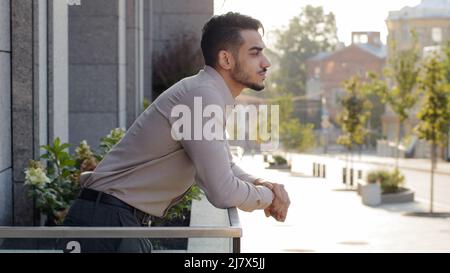 Glücklich nachdenklich erfolgreichen entspannten Geschäftsmann hispanic Kerl männlichen arabischen Investor Geschäftsmann steht auf Terrasse Balkon im Bürogebäude im Hotelzimmer Stockfoto