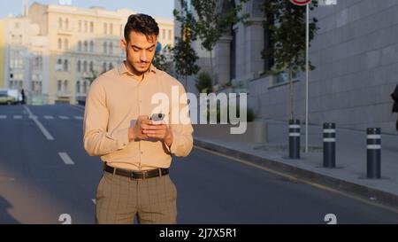 Stilvoller bärtiger hispanischer Geschäftsmann steht in der Innenstadt Straße nutzt Handy-SMS-Scrolling-Tapping-App-Technologie Online-Kommunikation mit Stockfoto