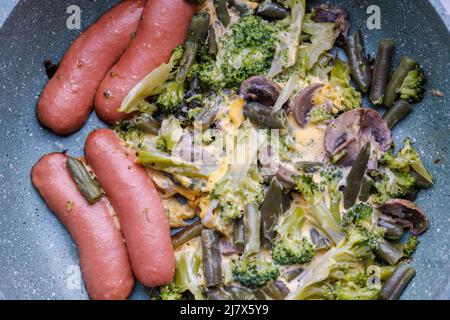 Gebratene Würstchen und Gemüse mit Pilzen und Hühnereier auf einer Pfanne Stockfoto