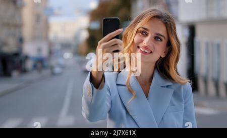 Porträt von jungen schönen Mädchen kaukasischen Geschäftsfrau Blogger Vlogger Modell steht in der Stadt hält Telefon Foto auf Handy-Kamera schießt Video Stockfoto