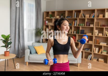 Schlanke junge koreanische Frau Heben Hanteln mit Training zu Hause, kümmert sich um den Körper am Morgen Stockfoto