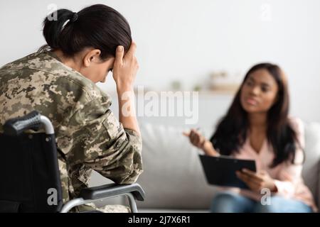 Unglückliche Soldatin mit Behinderung, die an einer Therapiesitzung mit einer schwarzen Psychiaterin teilnimmt Stockfoto