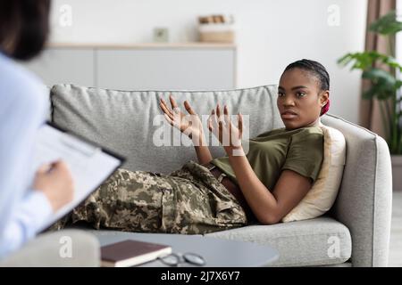 Schwarze Soldatin, die auf der Couch liegt und der Psychotherapeutin Probleme erklärt Stockfoto