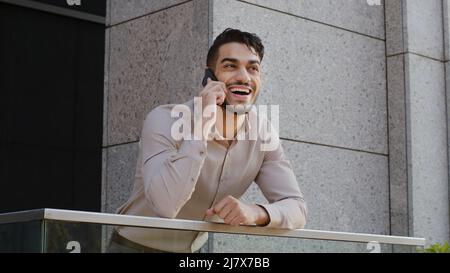 Porträt von fröhlich lächelnd sorglos glücklich hispanisch arabisch bärtig Geschäftsmann Chef Führer Kerl auf Balkon Terrasse stehen im Gespräch auf Handy Stockfoto