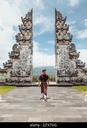 Junger, männlicher Tourist mit einem traditionellen balinesischen Sarong, der vor den Toren des Himmelstempels im Norden von bali, indonesien, läuft Stockfoto