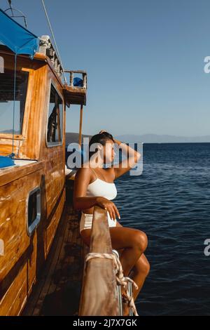 Junge asiatische weibliche Model sitzt auf der Seite eines Segelbootes in der ägäis von Bodrum Türkei an einem sonnigen Sommertag Stockfoto