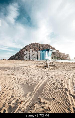 Blue Lifeguard steht am Morro Beach während des Sonnenuntergangs in Kalifornien mit Morro Rock in der Ferne Stockfoto