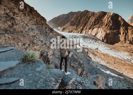 Junger Mann auf einem Felsen mit Blick auf den Passu-Gletscher im Norden von Hunza, Pakistan Stockfoto