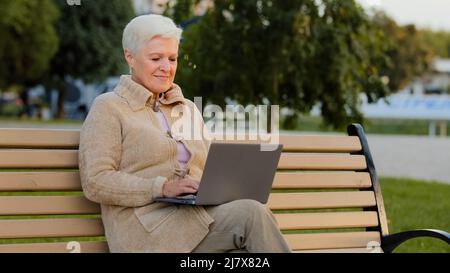 Schöne glückliche ältere Frau mit Laptop-Computer im Freien mittleren Alters Geschäftsfrau tippen auf der Tastatur und lächeln, ältere Dame im Internet surfen oder Stockfoto