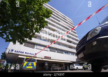 Hanau, Deutschland. 11.. Mai 2022. Vor einem Hochhaus, in dem am Morgen ein totes Mädchen gefunden wurde, hängt ein Polizeiflatterband. Vor dem Haus auf der Straße befand sich ein schwer verletzter Junge, der später starb. Kredit: Frank Rumpenhorst/dpa/Alamy Live Nachrichten Stockfoto