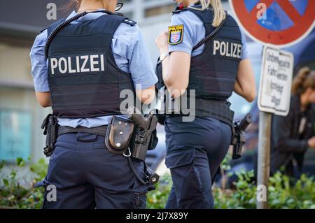 Hanau, Deutschland. 11.. Mai 2022. Zwei Polizeibeamte stehen vor einem Hochhaus, in dem am Morgen ein totes Mädchen gefunden wurde. Vor dem Haus auf der Straße befand sich ein schwer verletzter Junge, der später starb. Kredit: Frank Rumpenhorst/dpa/Alamy Live Nachrichten Stockfoto