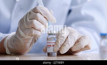 Nahaufnahme Frau Ärztin in Latexhandschuhen weibliche Hände des Mediziners Durchstechen Glasflasche mit Coronavirus-Impfstoff mit Nadel unter flüssigem Covid Stockfoto