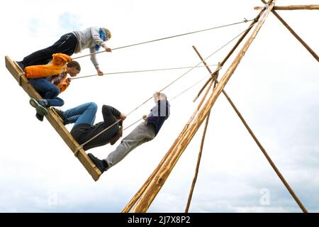 Russland, Tjumen, 15.06.2019. Kinder unterschiedlichen Alters und Schwingen auf dem großen altmodischen hölzernen Schaukeln, gegen den blauen Himmel mit Wolken. Stockfoto