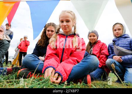 Russland, Tjumen, 15.06.2019. Eine Masse von Kindern unterschiedlichen Alters und Rennen sitzen auf dem Gras, in die Kamera schaut Stockfoto