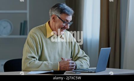 Nahaufnahme älterer Mann, der online verhandelt, Laptop-Professor, der Vortrag über das Internet lehrt zu Hause sitzend, Daumen hochzeigend, befriedigt die Arbeit im Ruhestand Stockfoto