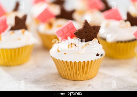 Gourmet-S'mores-Cupcakes mit Meringue-Zuckerguss und garniert mit sternförmiger Schokolade graham Cracker und einer pinken Mini-Tafel Schokolade. Stockfoto