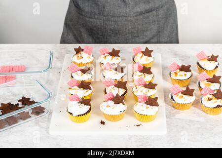 Gourmet-S'mores-Cupcakes mit Meringue-Zuckerguss und garniert mit sternförmiger Schokolade graham Cracker und einer pinken Mini-Tafel Schokolade. Stockfoto