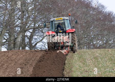 Ein Bauer, der an einem bewölkten Tag in der schottischen Landschaft ein Hillside Field pflügt Stockfoto