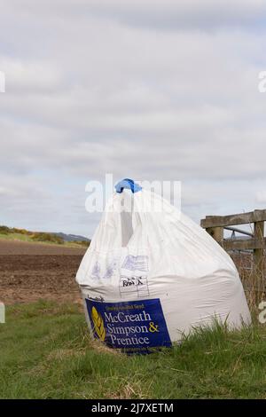 Ein Sack Gerste von einem Samenhändler am Tor zu einem Feld bereit, gesät zu werden. Stockfoto