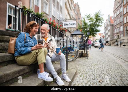 Fröhliche ältere Touristen, die auf Treppen sitzen und Kaffee im Freien in der Stadt trinken Stockfoto