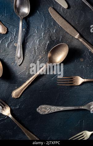 Besteck flach legen. Löffel, Gabeln und Messer, verschiedene Tischutensilien, von oben auf schwarzem Hintergrund geschossen Stockfoto
