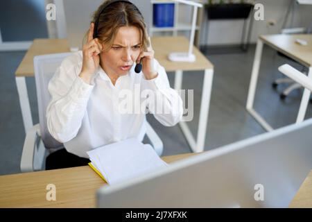 Erwachsene Callcenter-Telefonistin in einem Headset, das gestresst aussieht Stockfoto