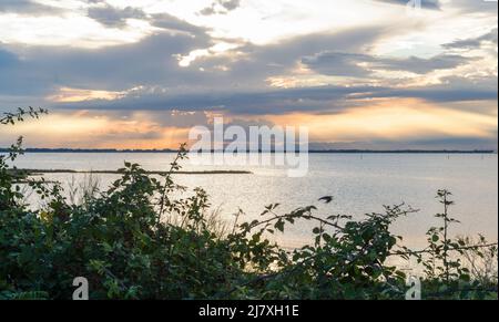 Schöner und friedlicher Sonnenuntergang über dem Meer mit blauen Wolken und orangefarbener Sonnenreflexion im Wasser Stockfoto