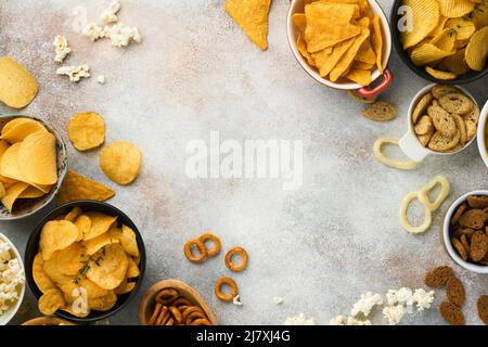 Snacks. Ungesunde Lebensmittel. Alle klassischen Kartoffelsnacks mit Erdnüssen, Popcorn- und Zwiebelringen und gesalzenen Brezeln in Schüsseln auf grauem Beton-Hintergrund Stockfoto