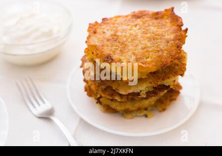 Gebratene Kartoffelpfannkuchen mit Sauerrahm auf weißem Teller Stockfoto