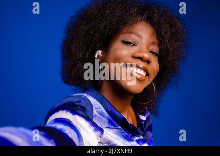 Nahaufnahme der schönen afrikanischen Dame, die lächelt, während sie ein Foto auf ihrem Handy macht Stockfoto