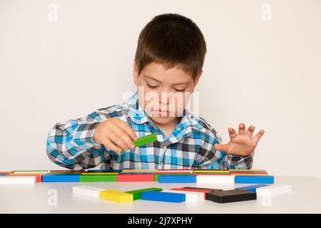 Ein Vorschulkind spielt mit mehrfarbigen Holzblöcken zum Bauen oder Zählen, die auf weißem Hintergrund an einem Tisch sitzen Stockfoto