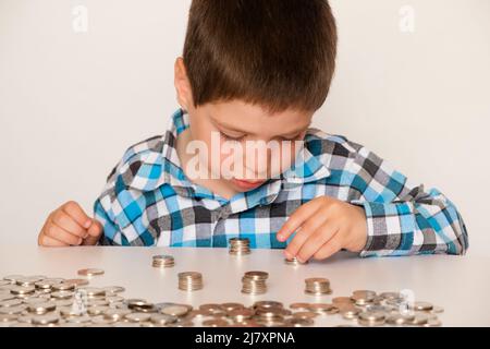 Ein Vorschuljunge in einem karierten Hemd zählt Münzen, baut Türme. Finanzielle Bildung für Kinder. Stockfoto