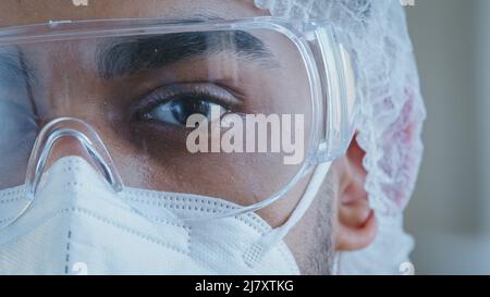 Nahaufnahme männlich schwarz müde und müde Auge Halbgesicht Mann Arzt trägt persönliche Schutzbrille medizinische Spezialkleidung Uniform arbeitet im Krankenhaus Stockfoto