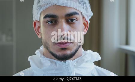 Portrait von erschöpften müde junge arabische Arzt Krankenschwester Praktiker in Schutzuniform Latex Handschuhe steht in der Klinik nimmt medizinische Kappe aus Stockfoto