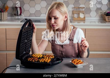 Frau, die frische Waffeln aus dem Waffeleisen in der Küche mit belgischen Waffeln nahm Stockfoto