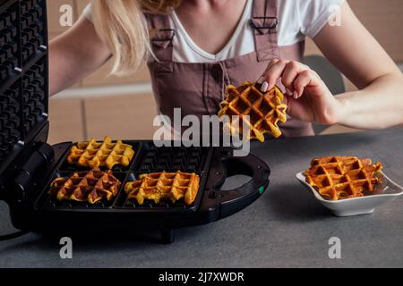 Frau, die frische Waffeln aus dem Waffeleisen in der Küche mit belgischen Waffeln nahm Stockfoto