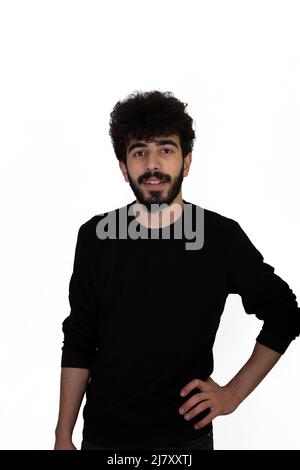 Lockig behaarte junge Rüde in schwarzem Pullover mit einer Hand auf der Hüfte. Isoliert auf weißem Hintergrund Stockfoto