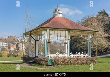 Quadratisches, reich verziertes Band steht in einem weiß und grün gestrichenen Park mit einem Ziegeldach vor einem blauen Frühlingshimmel Stockfoto