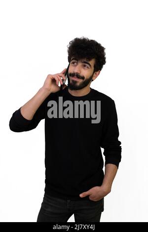 Lockig behaarte junge Rüde in schwarzem Pullover, die lächelnd auf dem Handy reden. Isoliert auf weißem Hintergrund Stockfoto