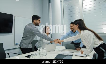 Aufgeregte multikulturelle, fröhliche Geschäftsleute, die bei einem Treffen zusammen sitzen und hohe fünf Gesten geben, fühlen sich multiethnische Kollegen glücklich und zeigen dem Team Stockfoto