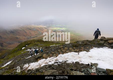 Wanderer, die im Spätwinter den Weg zum Gipfel des Old man of Coniston im Lake District National Park, Cumbria, England, besteigen. Stockfoto