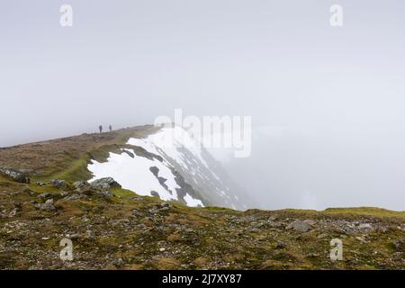 Wanderer in niedrigen Wolken auf dem Gipfel des Old man of Coniston im Spätswinter im Lake District National Park, Cumbria, England. Stockfoto