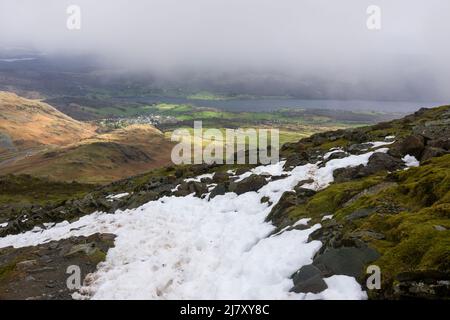 Schnee auf dem alten Mann von Coniston mit dem Dorf Coniston und Coniston Wasser unten im späten Winter im Lake District National Park, Cumbria, England. Stockfoto