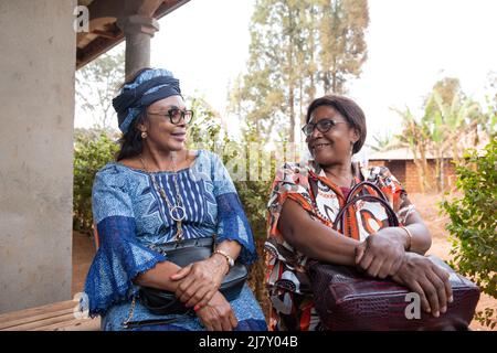 Zwei ältere afrikanische Freundinnen sitzen und plaudern, afrikanische Frauen traditionell gekleidet, Freundschaftskonzept für Erwachsene Stockfoto