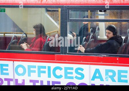 Passagiere, einige tragen eine Maske, andere nicht, werden in einem Doppeldeckerbus in der City of London gesehen. Stockfoto