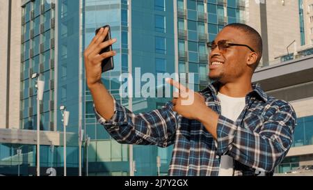 Porträt des amerikanischen Mannes in Sonnenbrille männlichen Touristen macht Videoanruf Handy-App in der Stadt stehend zeigt Gebäude Hintergrund spricht Smartphone Stockfoto