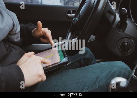 Der Vertriebsmitarbeiter fährt mit einem Tablet in den Händen, die Hände am Lenkrad im Auto, arbeitet Stockfoto