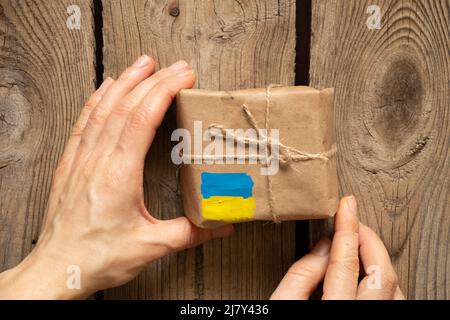 Eine Schachtel mit einer gelb-blauen Flagge der Ukraine in der Hand einer Frau, humanitäre Hilfe für die Ukraine von Menschen Stockfoto