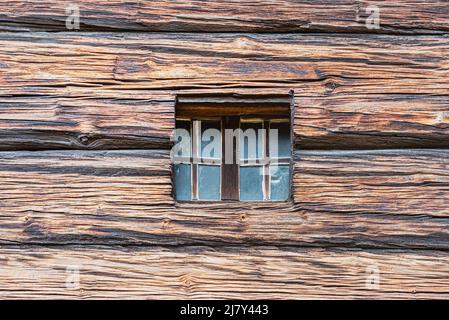 Quadratisches kleines Fenster in einer alten Holzoberfläche oder Fassade geschnitzt. Detail von niedlichen winzigen Fenster auf einem Holz - gemacht oder Fachwerk außen eines wikingerhauses Stockfoto